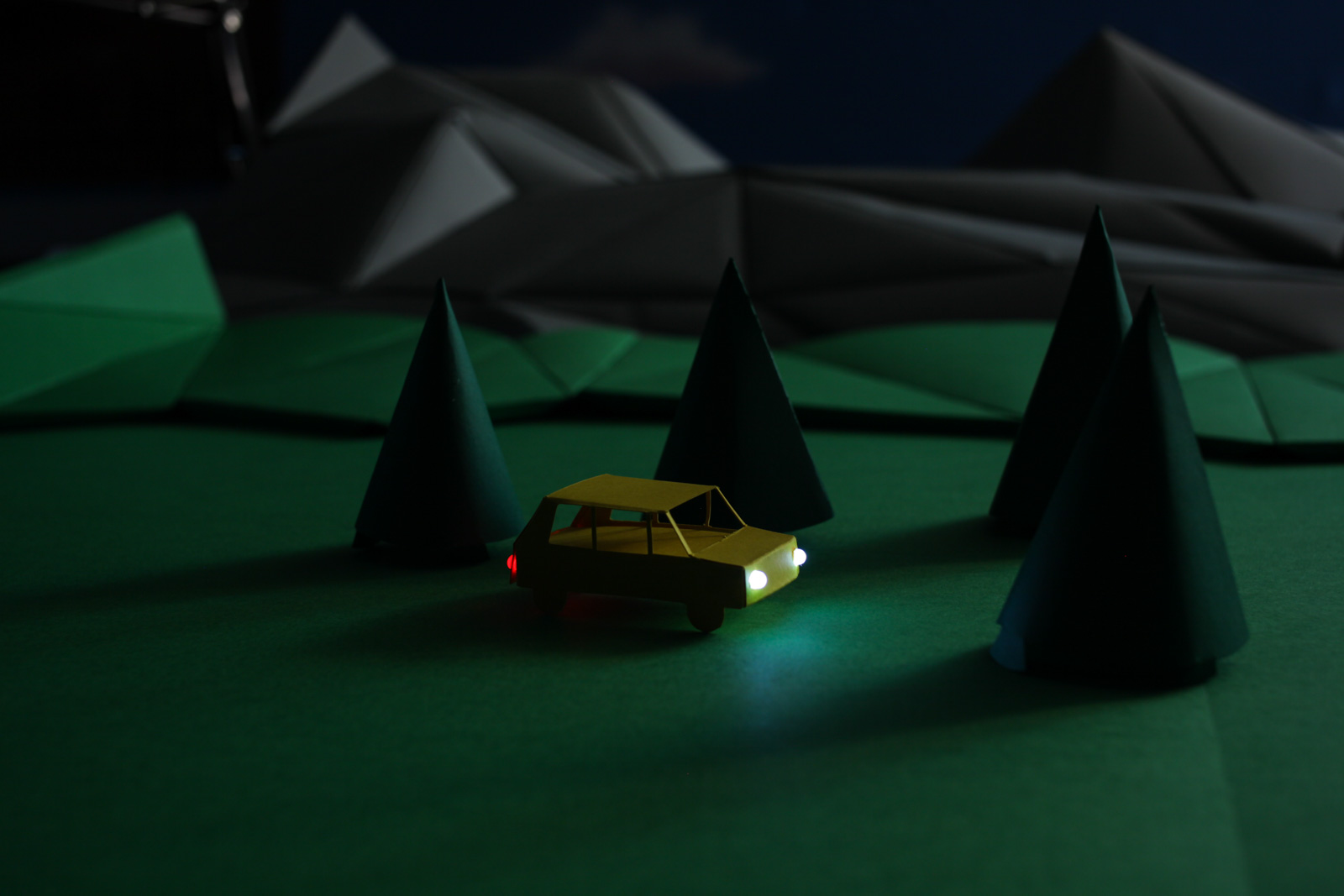 Papierauto mit Beleuchtung in dunkler Landschaft.