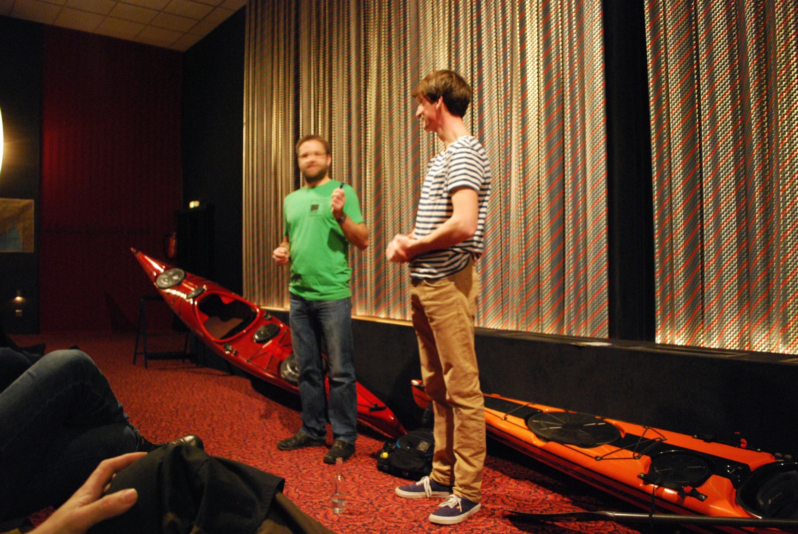 Zwei Männer stehen vor einer Kinoleinwand und moderieren einen Film an.