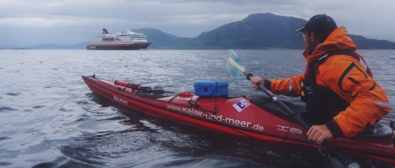 Sea Kayak paddling in a fjord with Hurtigruten cruise ship in the background.