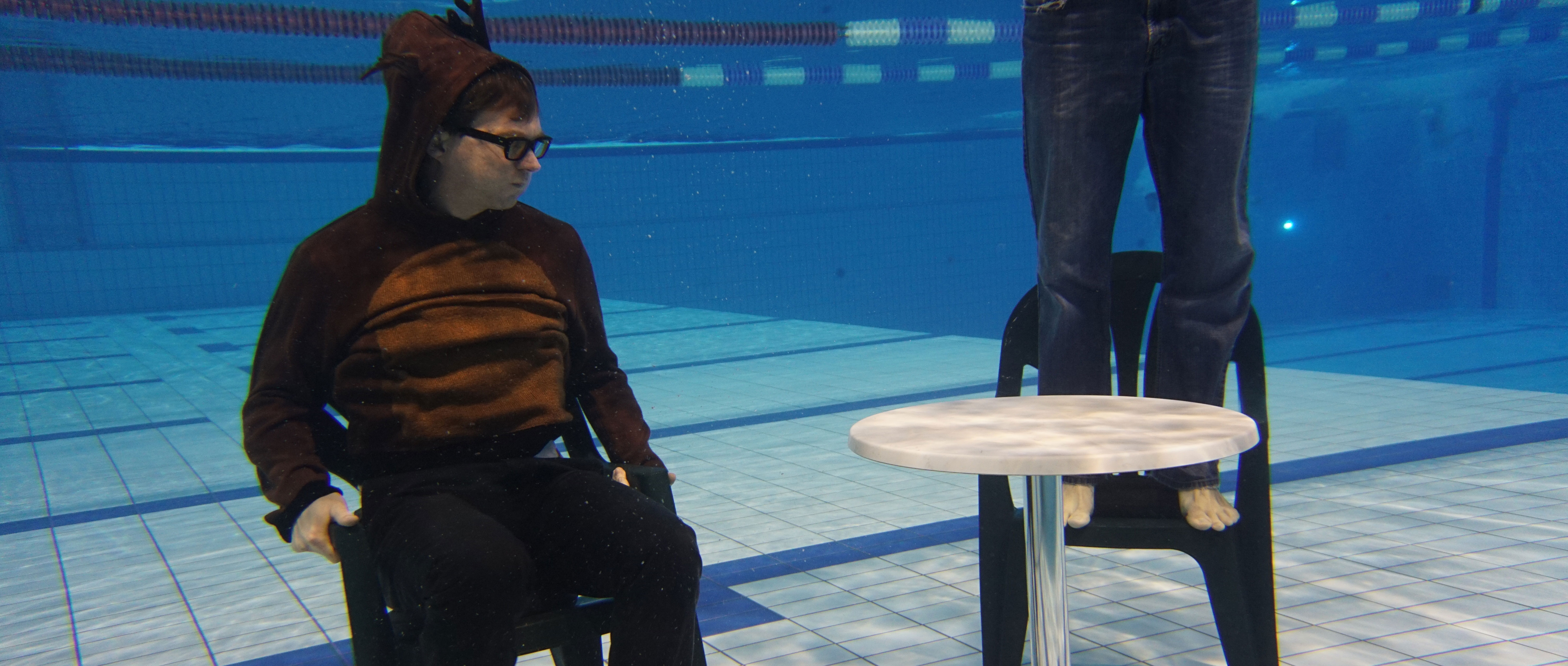Ein Mann im Renntier Kostüm, hält die Luft an und sitzt Unterwasser an einem Tisch.