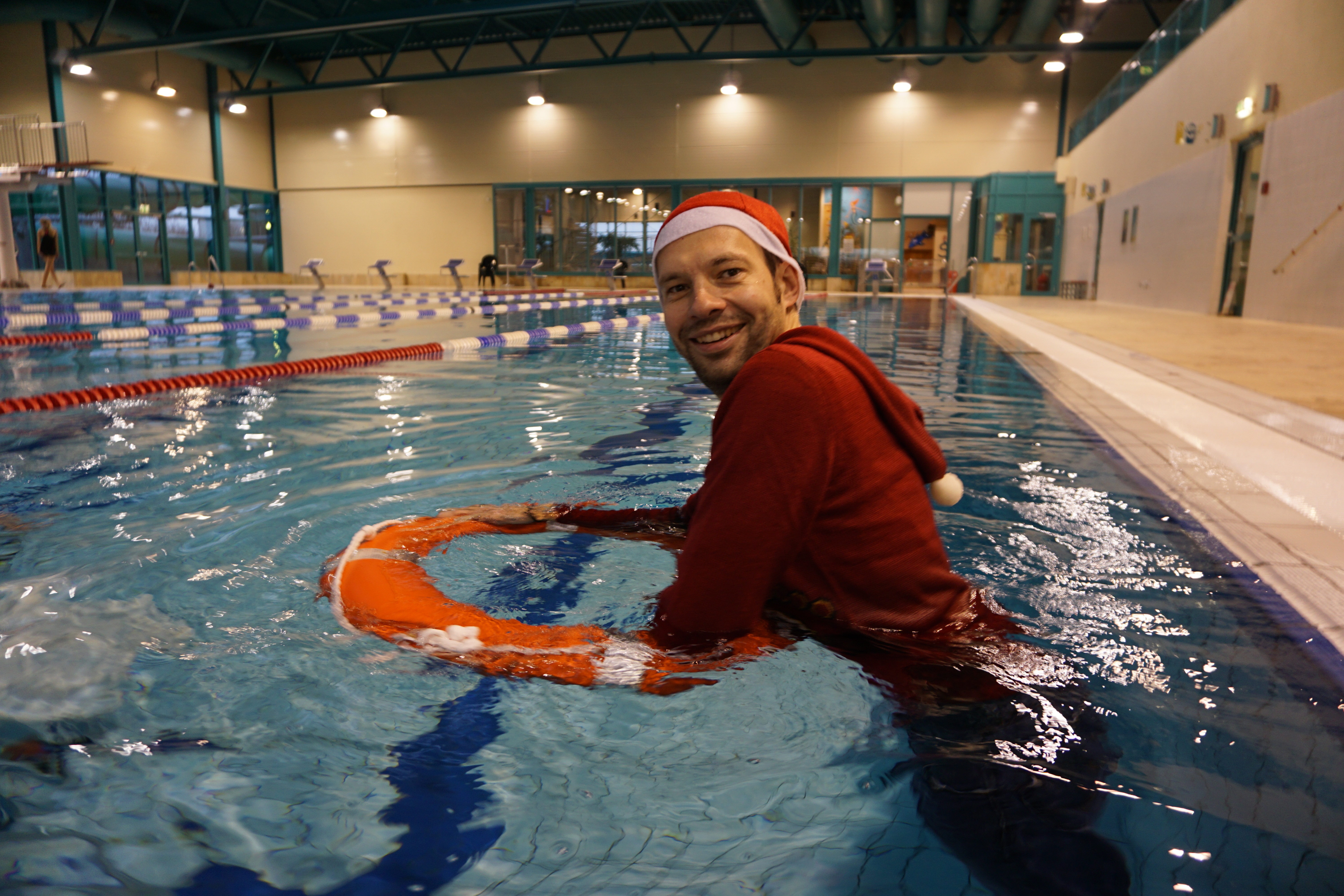 Kristof in Weihnachtsverkleidung hält sich lächelnd an einen Rettungsring im Schwimmbad.