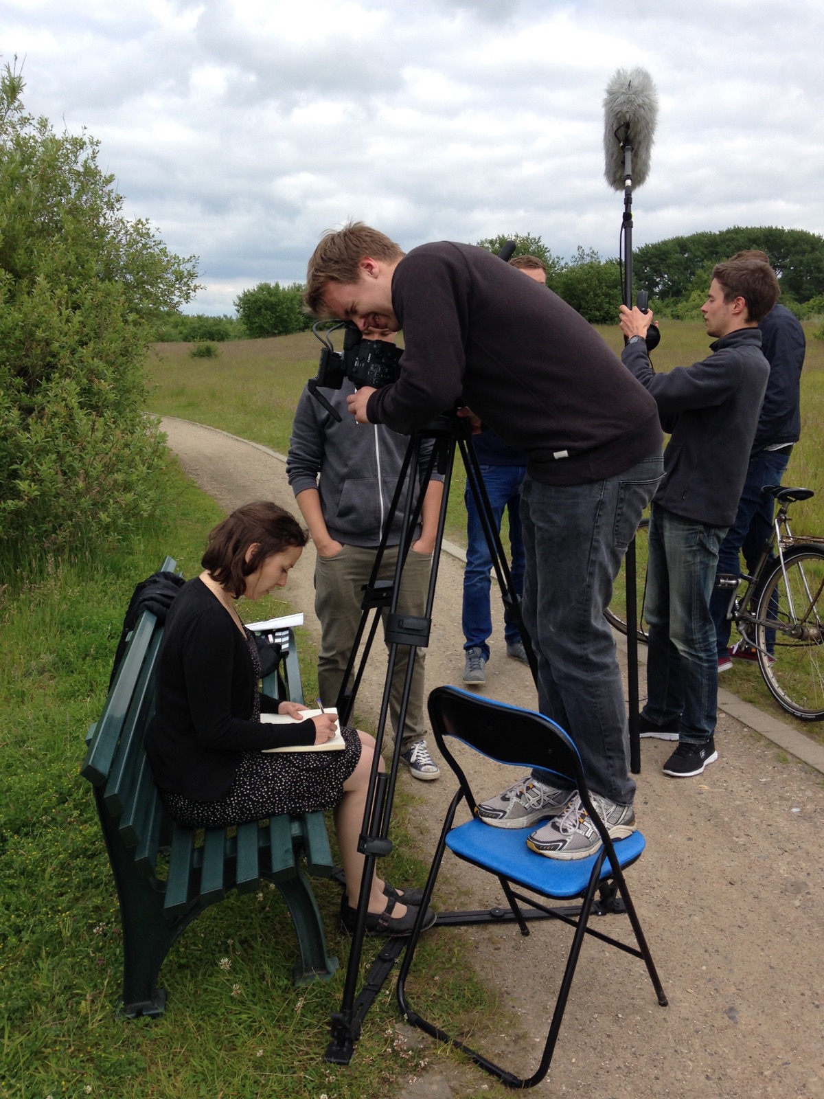 Kameramann Niels-Jonas filmt auf einem Stuhl stehen, wie eine Frau etwas auf einen Block schreibt.