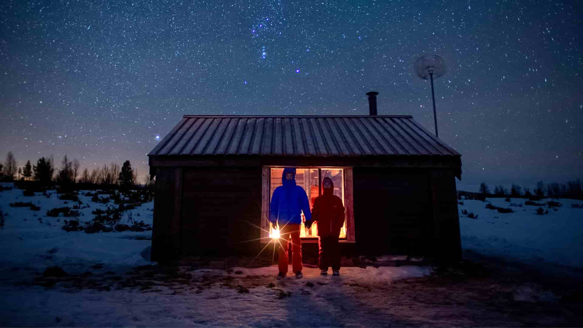 Old cabin in snow and star lighted sky.