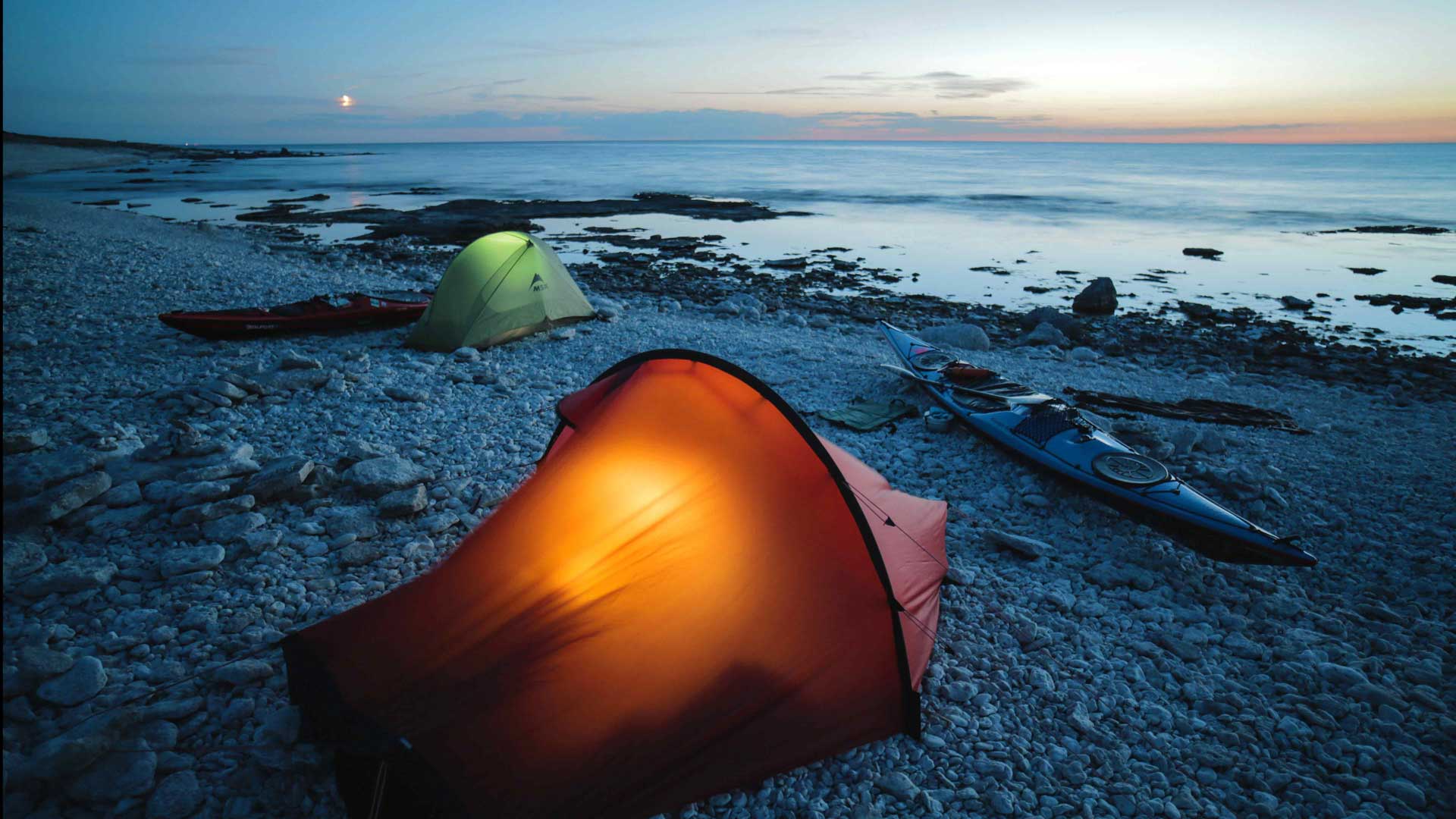 Orange tent in the sunset on a rocky beach.