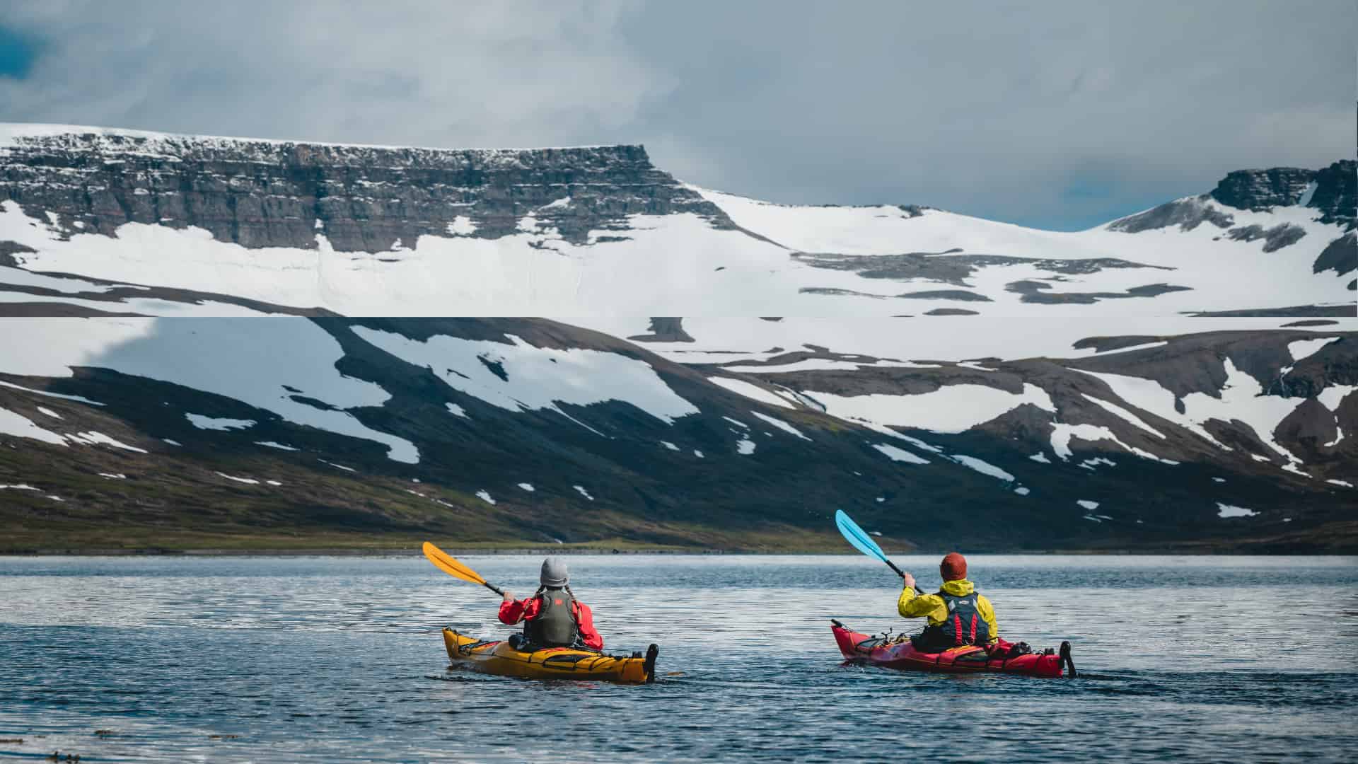 Two kayaks heading towards a snow covered mountain.