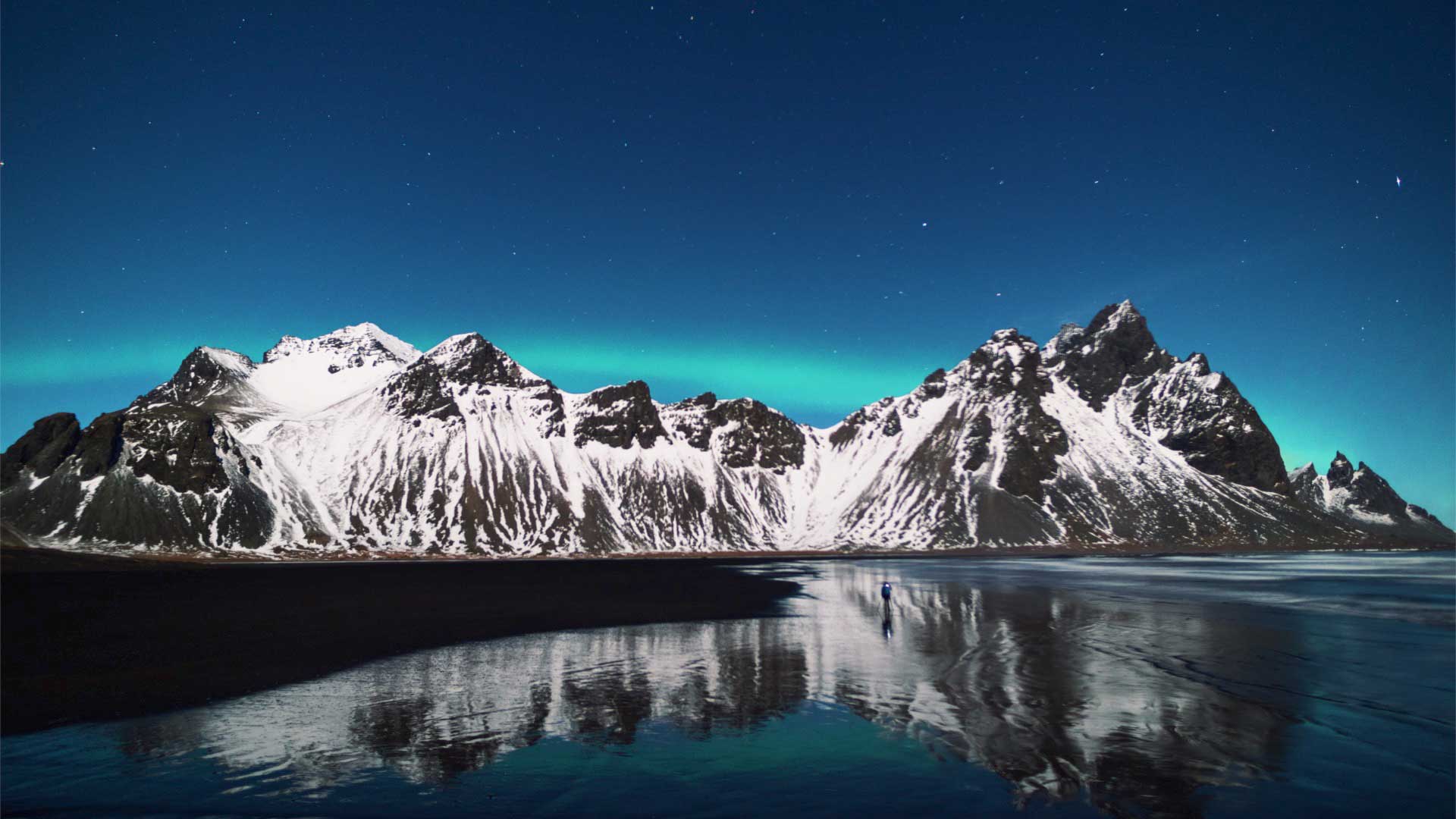 Northern lights above mountainins and mirrored in the sea.