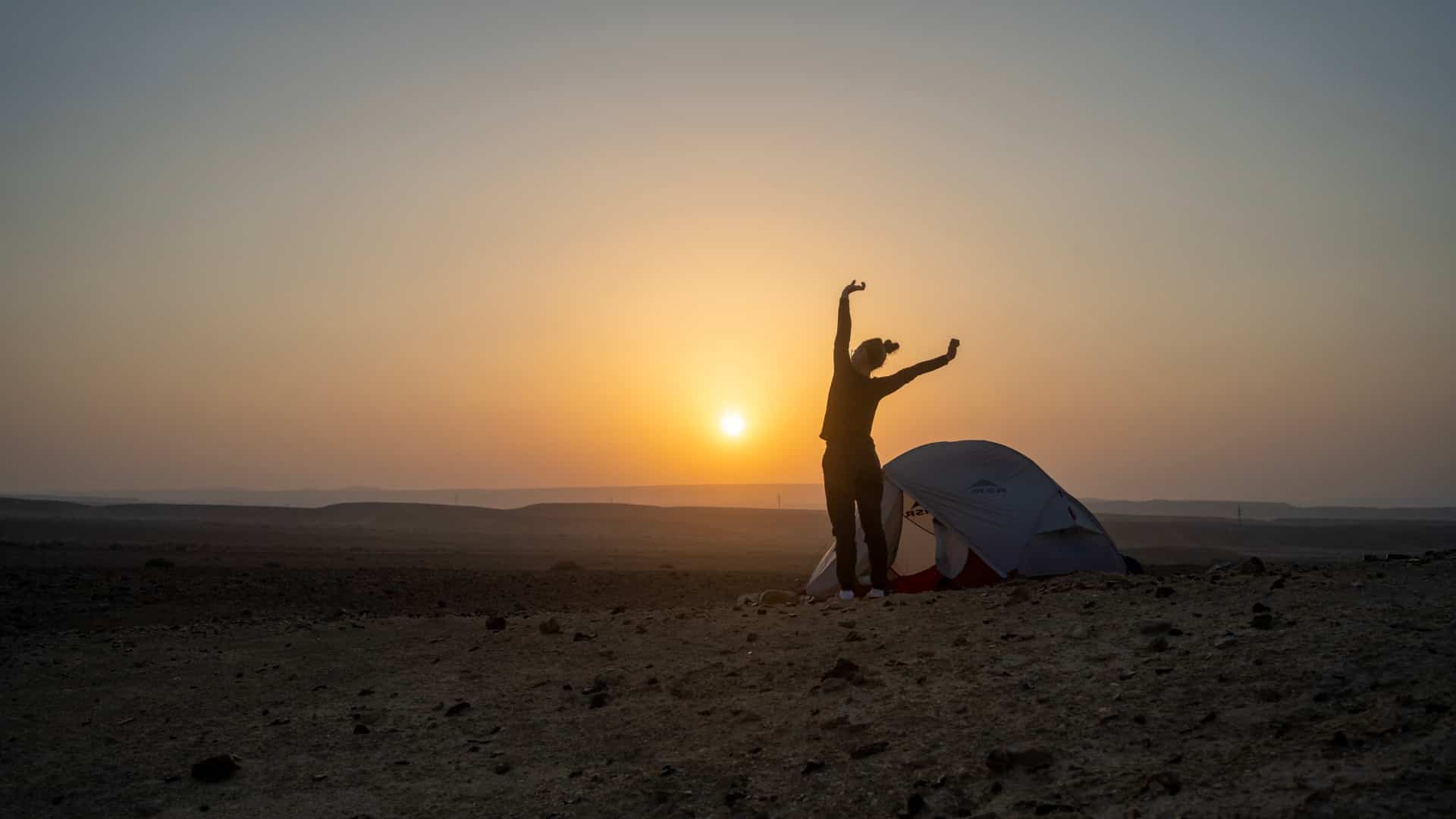 Young woman streching next to a tent in the desert during sunrise.